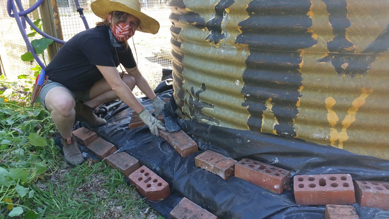 Meg uses black plastic to heat treat the grass embedded around the water tank.